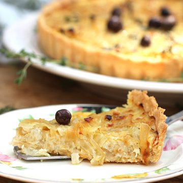 Close up of a slice of French onion tart with a nicoise olive on top, the rest of the tart in the background