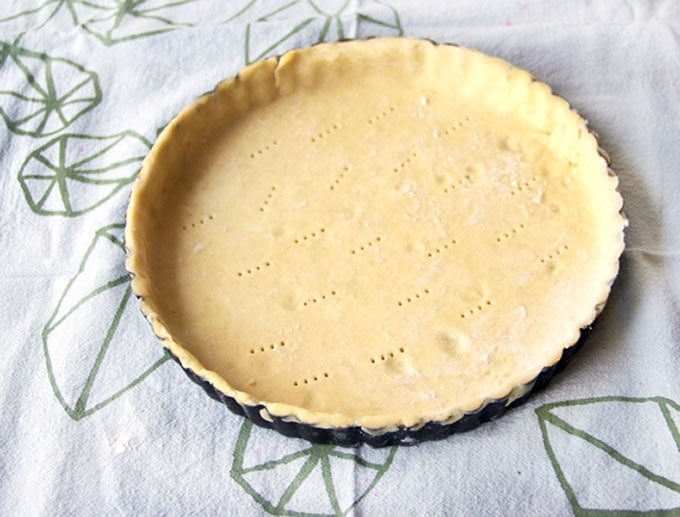 A tart pan lined with raw pie crust that has been poked several times with a fork