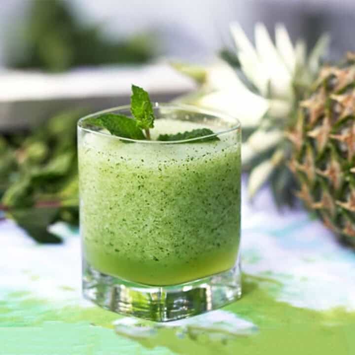 Frozen mojito in a glass with a mint sprig garnish and a pineapple behind it.