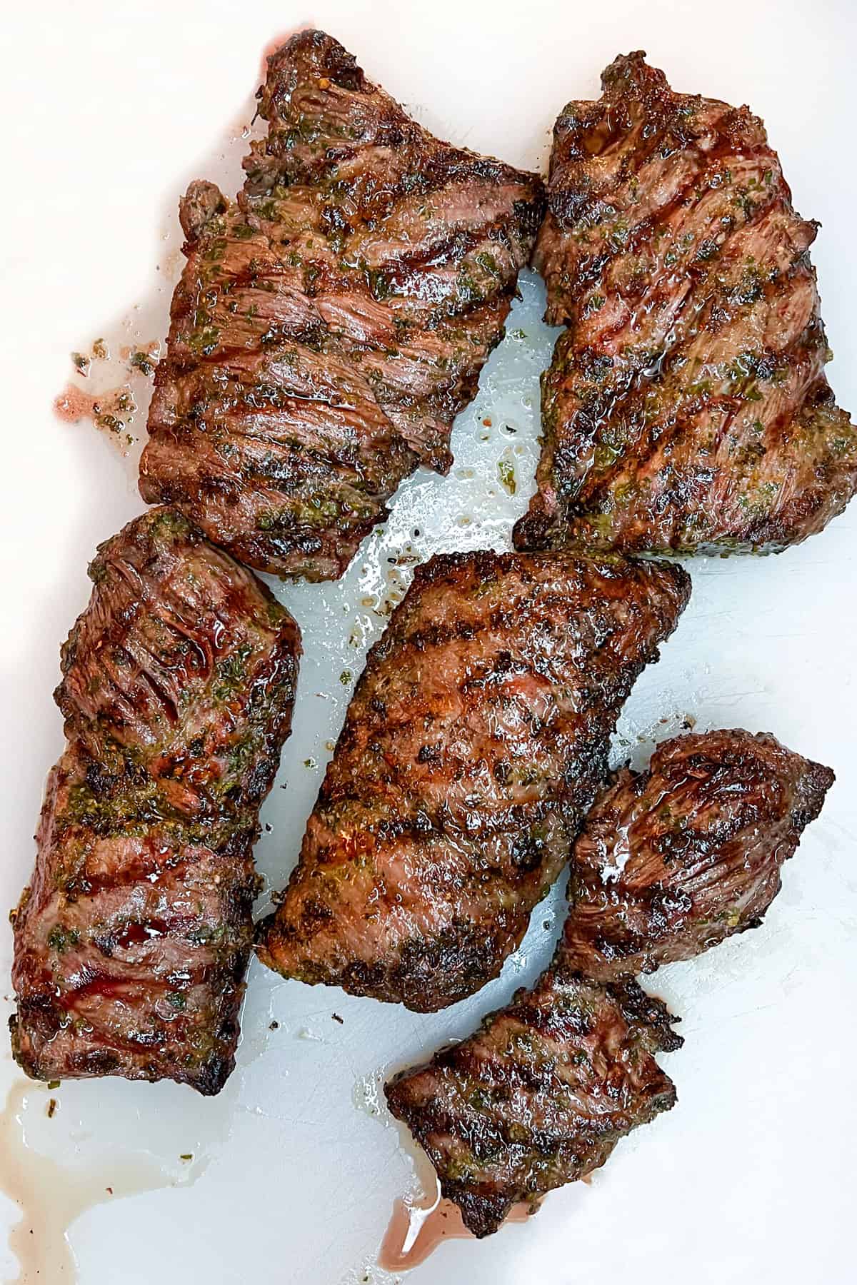 5 pieces of grilled skirt steak on a white cutting board seen from above