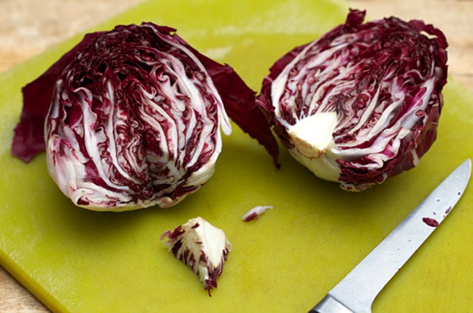 A head of radicchio sliced in half, one half with the triangular core cut out of it, both halves sitting on a pea green cutting board