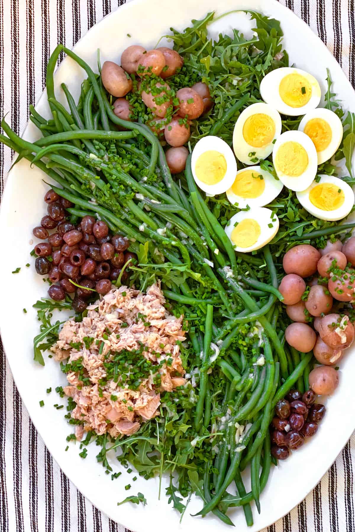 white platter topped with salad nicoise: tuna, small red potatoes, sliced hard boiled eggs, nicoise olives and French green beans