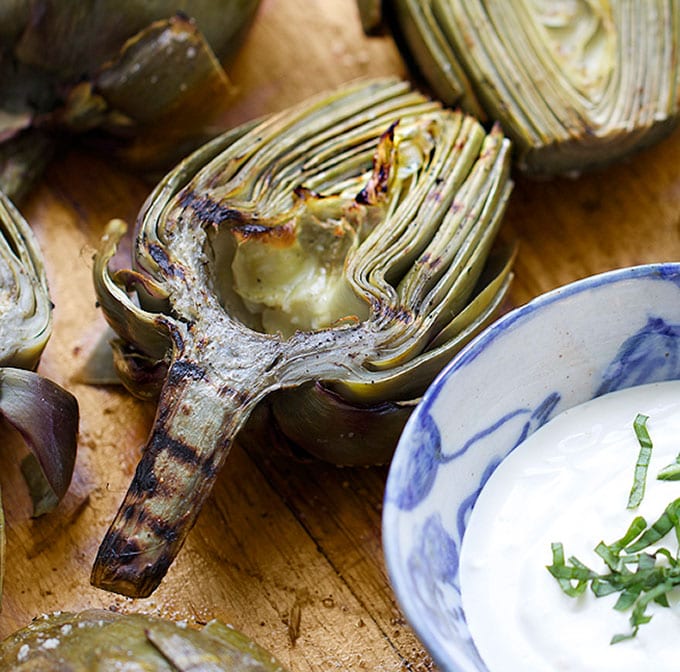 Grilled artichoke half next to a small bowl of lemon aioli.