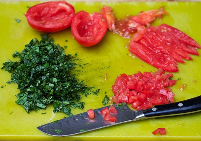 tomatoes and herbs on a chopping board to prep for three bean salad