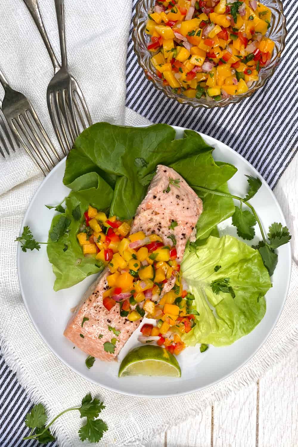 Broiled salmon on butter lettuce topped with mango salsa, several forks on the side and a small bowl of salsa on the side