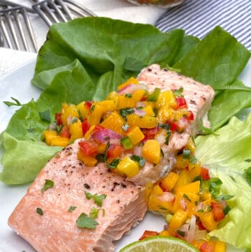 A piece of broiled salmon fillet on a bed of butter lettuce and topped with mango salsa