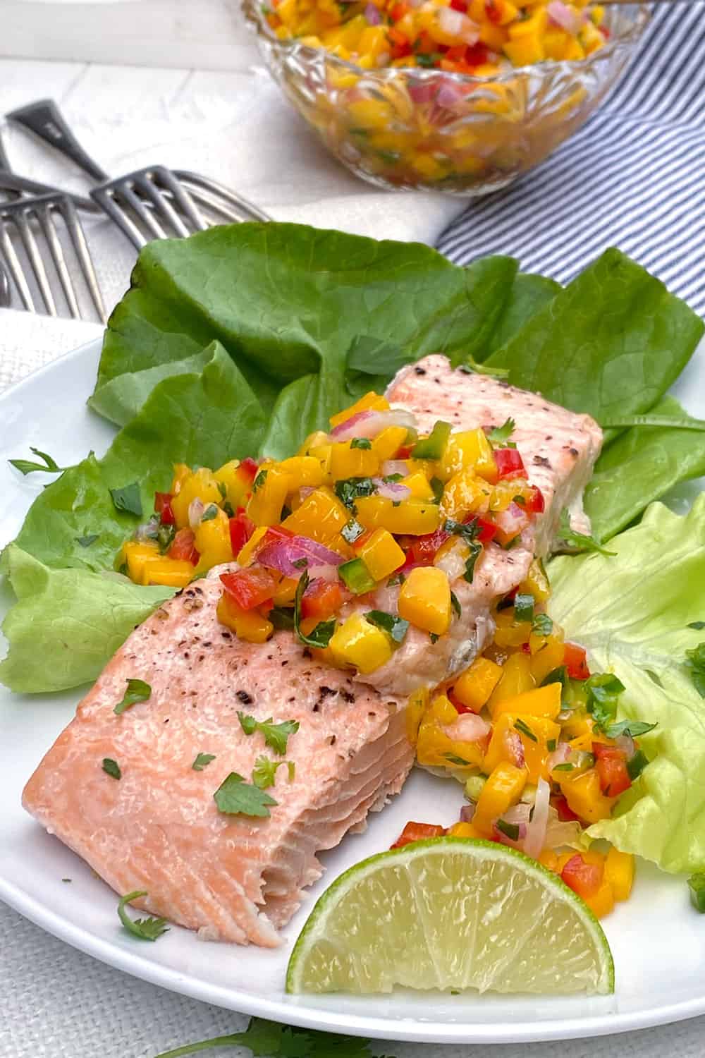 A piece of broiled salmon fillet on a bed of butter lettuce and topped with mango salsa