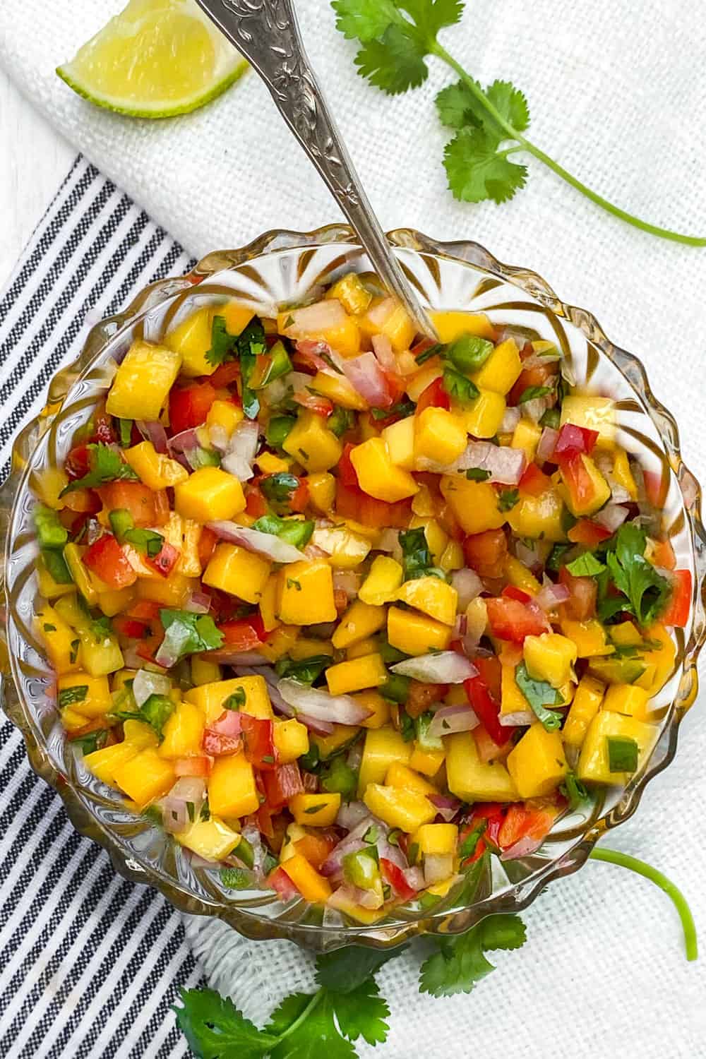 glass bowl filled with colorful mango salsa, a slice of lime and a couple of cilantro sprigs on the side