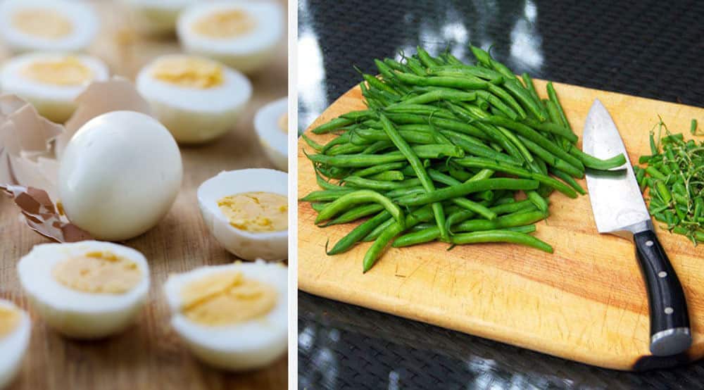 A bunch of hard boiled eggs on a counter, one peeled and whole, the others halved, and a cutting board with a pile of trimmed green beans on it