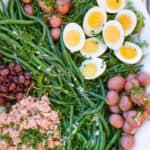 white platter topped with salad nicoise: tuna, small red potatoes, sliced hard boiled eggs, nicoise olives and French green beans