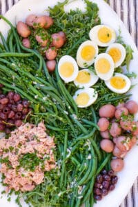 white platter topped with salad nicoise: tuna, small red potatoes, sliced hard boiled eggs, nicoise olives and French green beans