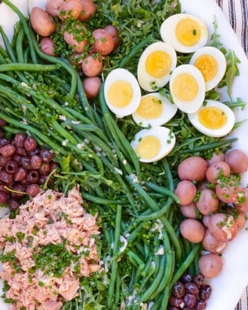 white platter topped with salad nicoise: tuna, small red potatoes, sliced hard boiled eggs, nicoise olives and French green beans