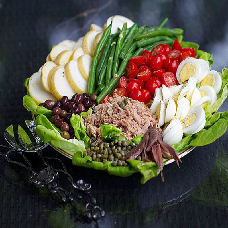 composed tuna nicoise salad with halved hard boiled eggs, canned tuna, cherry tomatoes, nicoise olive, steamed green beans, anchovies and sliced potatoes