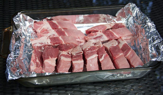 A glass baking dish lined with foil and filled with 13 individual baby back pork ribs