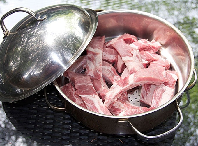 A stainless steel steamer pot filled with a dozen individual raw baby back pork ribs