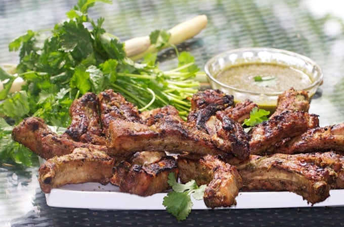 White platter piled high with barbecued baby back ribs, a pile of cilantro in the background