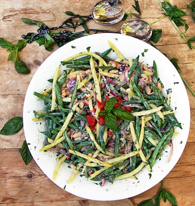 Big white bowl filled with colorful three bean salad with garnishes of basil leaves