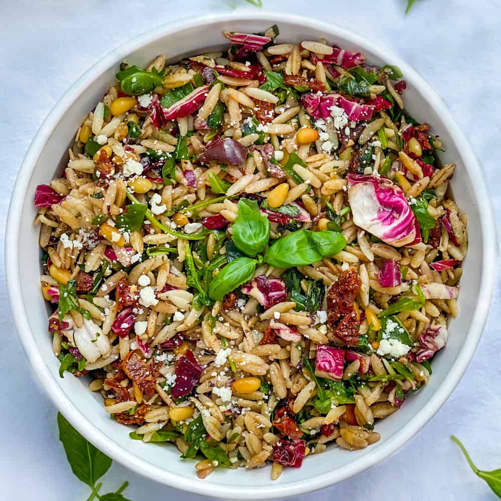 orzo pasta salad in a white bowl with a sprig of basil in the middle