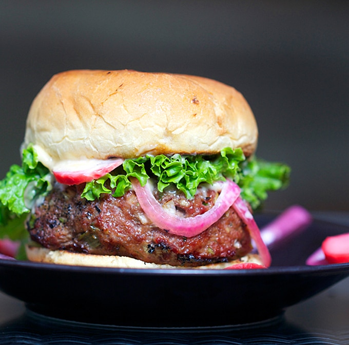 a Korean BBQ Burger in a bun with green leaf lettuce, pink pickled red onions and radishes