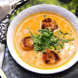 Bowl of coconut sweet potato soup topped with three spice crusted shrimp and shredded spinach in the center.