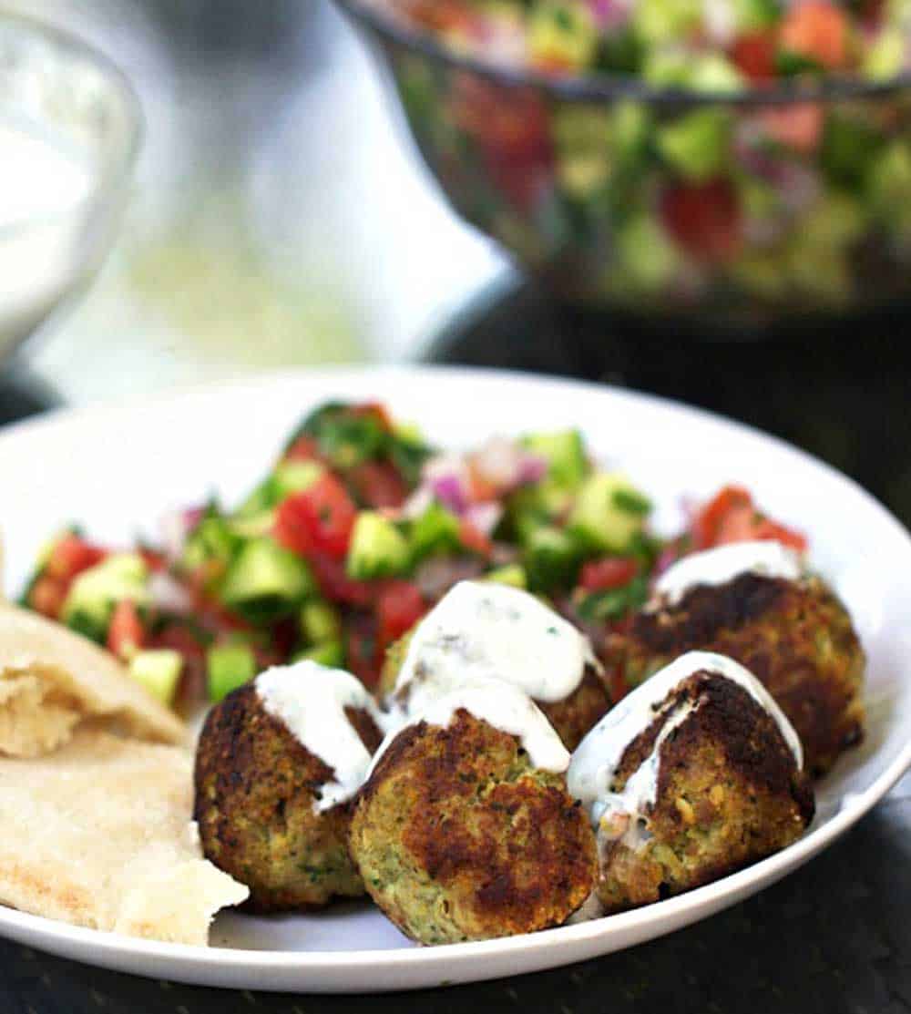 5 turkey falafel meatballs on a plate, drizzled with yogurt sauce