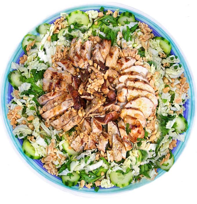 Round platter filled with a salad of shredded cabbage, cucumbers and mint, topped in the center with sliced grilled chicken, shiitake mushrooms and a sprinkle of chopped peanuts