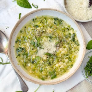 zucchini egg drop soup in a bowl topped with chopped basil and grated parmesan.