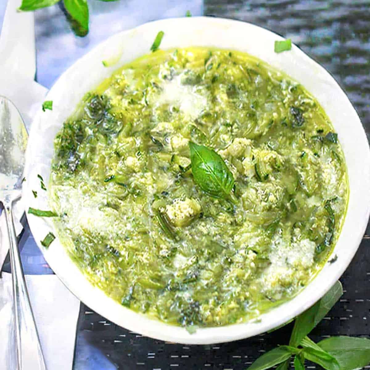 zucchini egg drop soup in a bowl with a basil leaf garnish.
