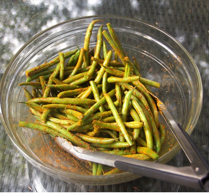 fresh green beans in a glass bowl with tongs, tossing the beans with Indonesian satay spices