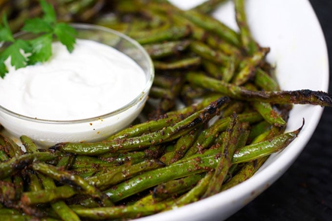 close up of grilled green beans and lemon aioli in a white bowl