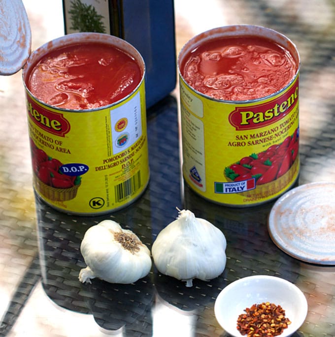 Ingredients for tomato sauce: cans of Italian plum tomatoes, bulbs of garlic.