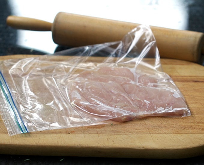 how to pound chicken for cutlets, a piece of chicken in a plastic bag on a cutting board and a rolling pin in the background