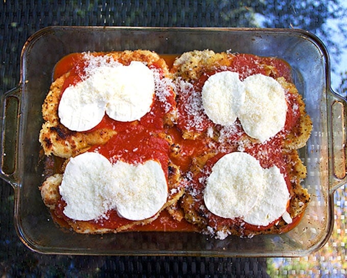 Glass baking pan with breaded chicken cutlets, tomato sauce and mozzarella cheese, showing How to make breaded chicken Parmesan