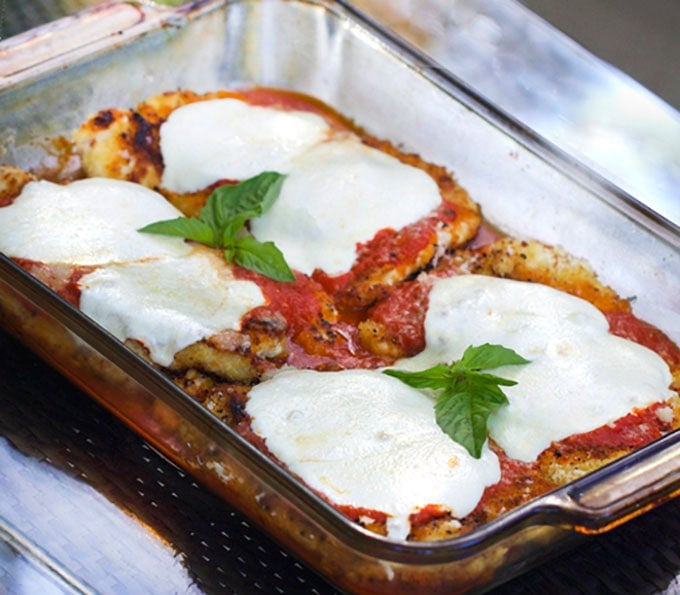 Breaded Chicken Parmesan just out of the oven with tomato sauce, melted cheese and two sprigs of fresh basil