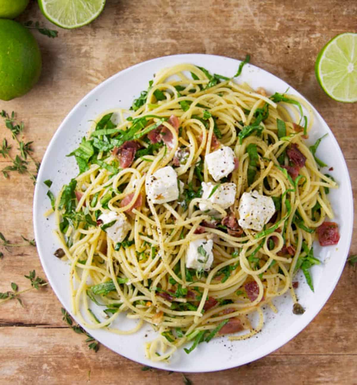 Plate of spaghetti twirled with slivered prosciutto and arugula, and topped with cubes of marinated feta.