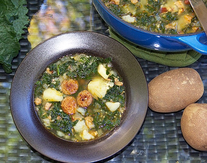 a bowl of sausage kale potato soup with a couple of russet potatoes o the side