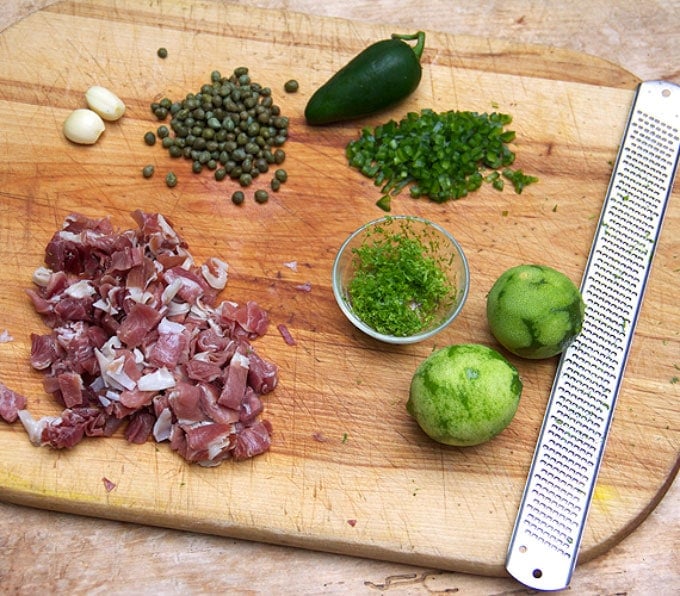 Ingredients on a chopping board: capers, garlic, lime zest, peppers