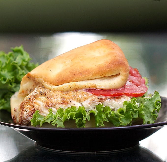 Grilled fish sandwich made on a fluffy coco bread roll with lettuce, a slice of tomato and jerk mayo.