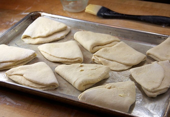 10 folded dough pieces on a rimmed baking sheet with a pasty brush in the background.