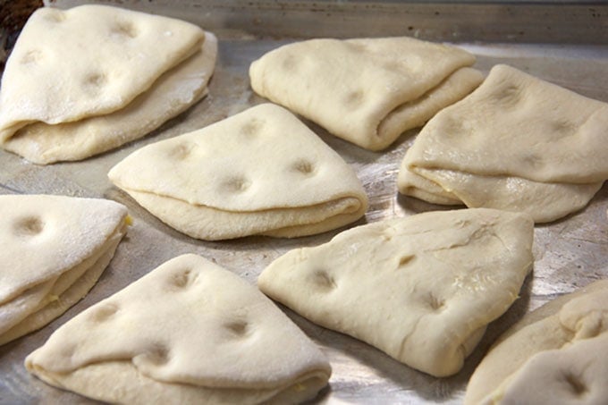 Uncooked dough formed into folded triangles and on a baking sheet, ready to go into the oven.