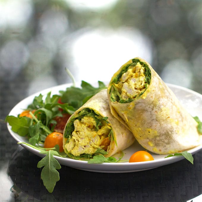 two curried Chicken Salad roll-ups in flour tortillas on a plate with arugula and cherry tomatoes