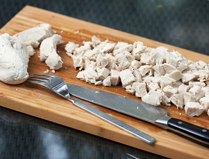 wooden cutting board with a fork, a knife and cubed poached chicken