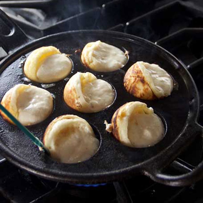 Showing how aebleskivers look after the first quarter turn, with a part that looks sperical and some raw batter pouring out from each partial sphere, into the hot pan.