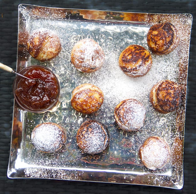 overhead looking down into a silver square platter topped with 10 aebleskiver dusted with powdered sugar, and a small bowl of strawberry jam to the side