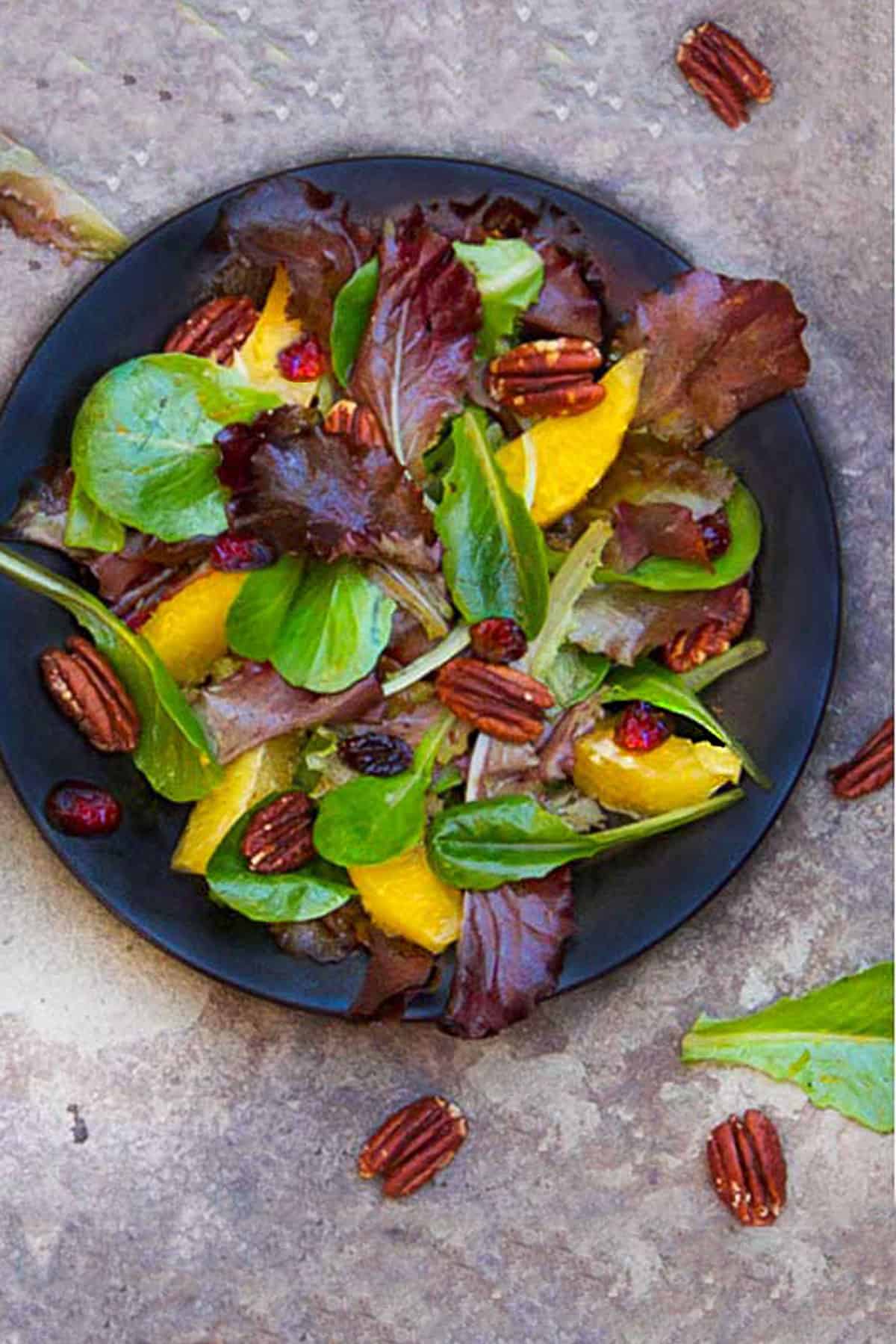 leafy salad on a small plate with baby romaine, orange segments, toasted pecans and cranberries.