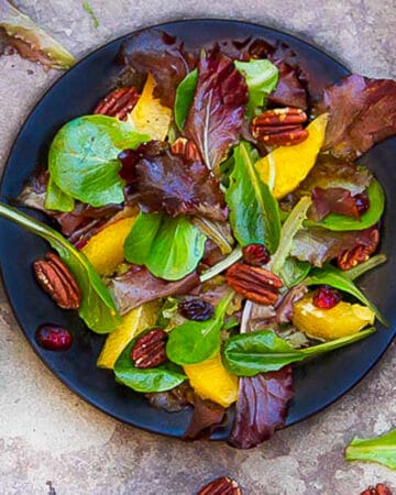 leafy salad on a small plate with baby romaine, orange segments, toasted pecans and cranberries.