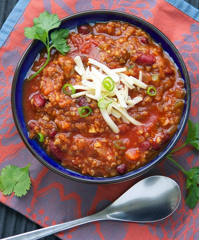 A royal blue bowl on a bright pink and blue napkin with a spoon and the bowl is filled with vegetarian chili.