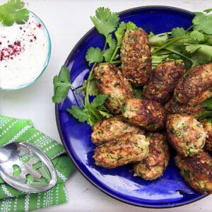a dozen or so turkey zucchini meatballs in a serving bowl with a small bowl of lemon yogurt dipping sauce on the side.