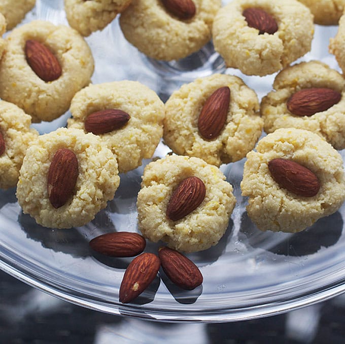 Close up of 7 flourless almond cookies on a glass plate with three almond decorating the edge of the plate