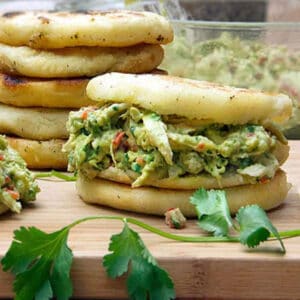 Arepas stuffed with chicken avocado salad, and a stack of five arepas in the background.